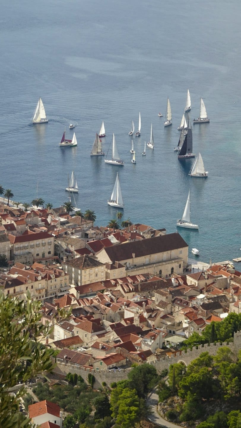 Vele da regata corrono lungo la costa di una storica cittadina marittima.