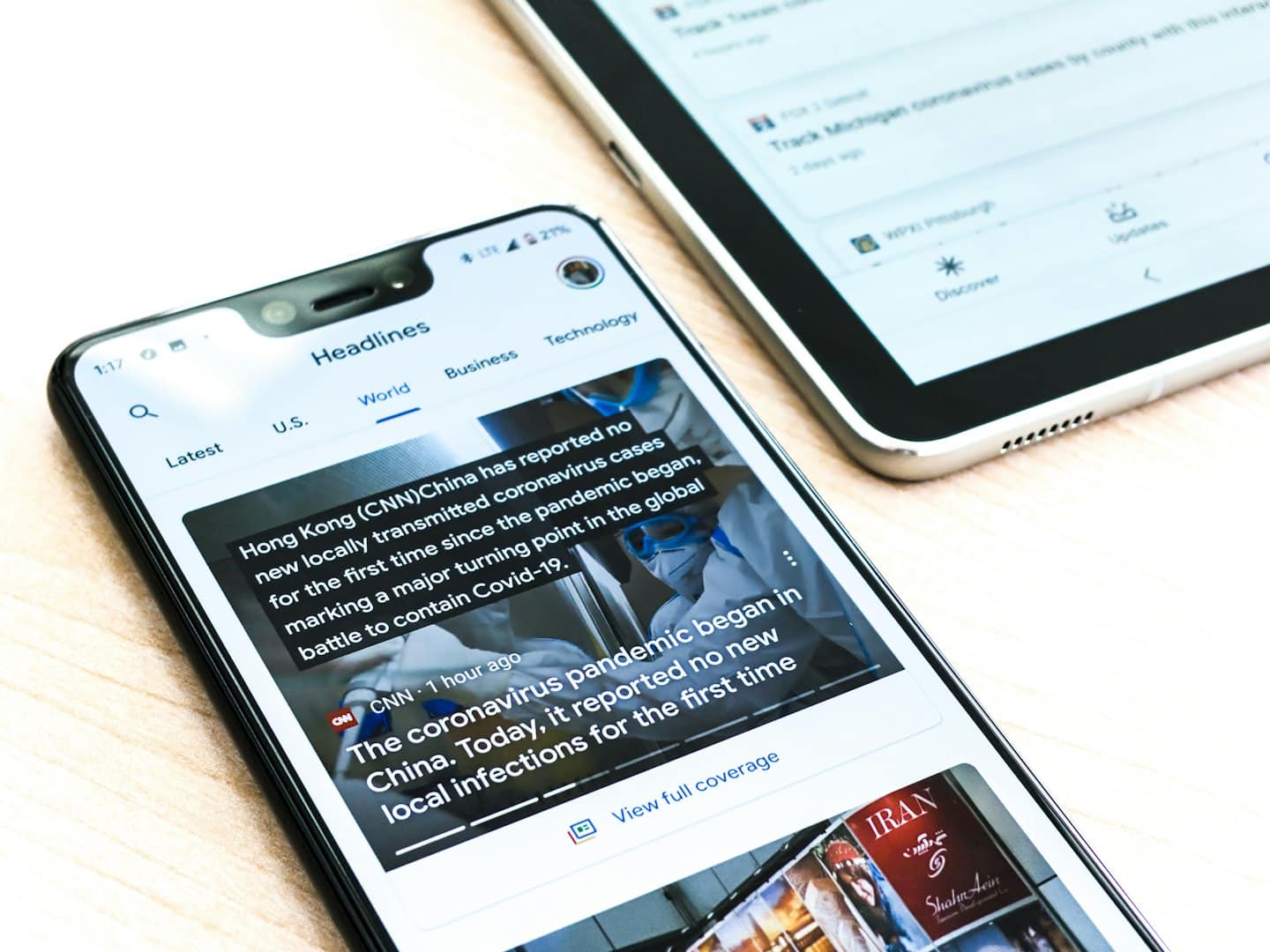 Smartphone e tablet che mostrano app di notizie su una scrivania di legno.