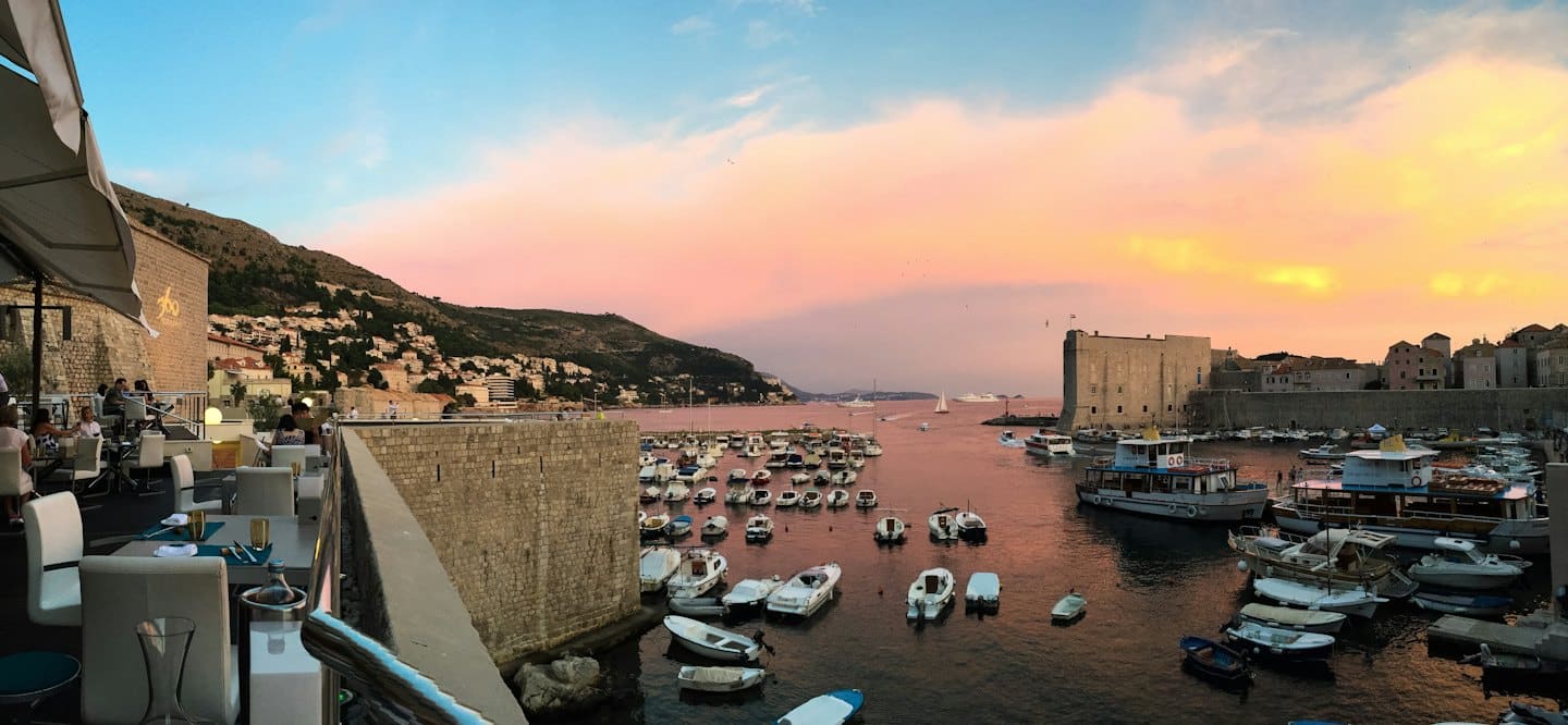 Clienti cenano con vista sul porto e sulle mura storiche.